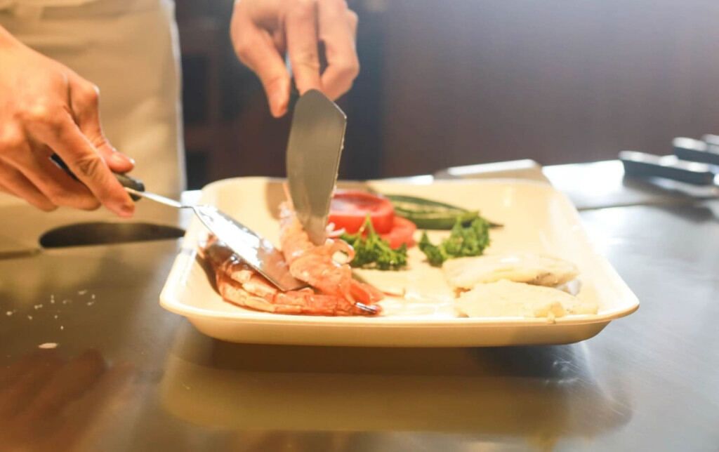 Hands serving a plated hot meal of meat and vegetables
